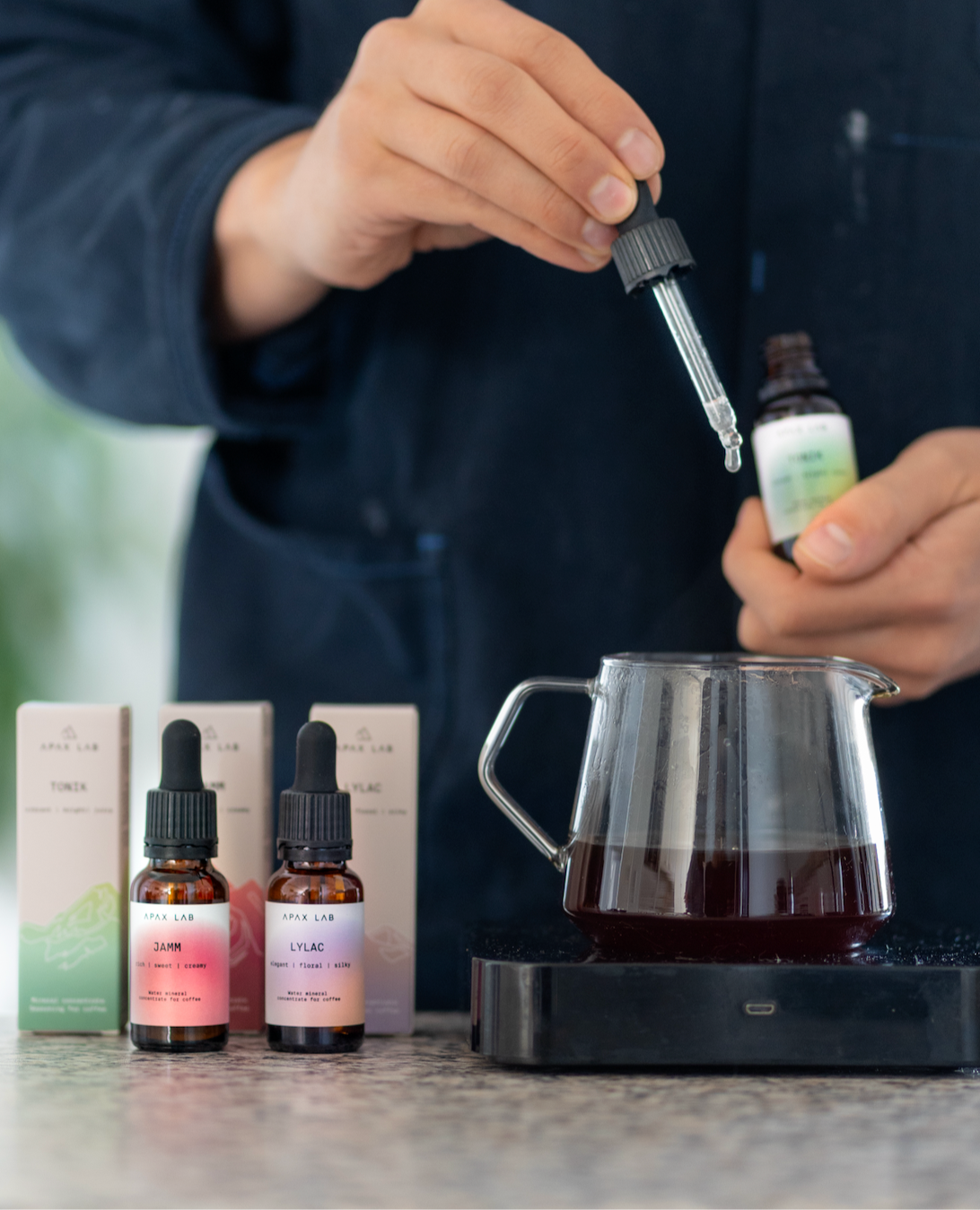 Barista adding drops of mineral concentrate into a brewed coffee. Featuring JAMM and LYLAC on the side.