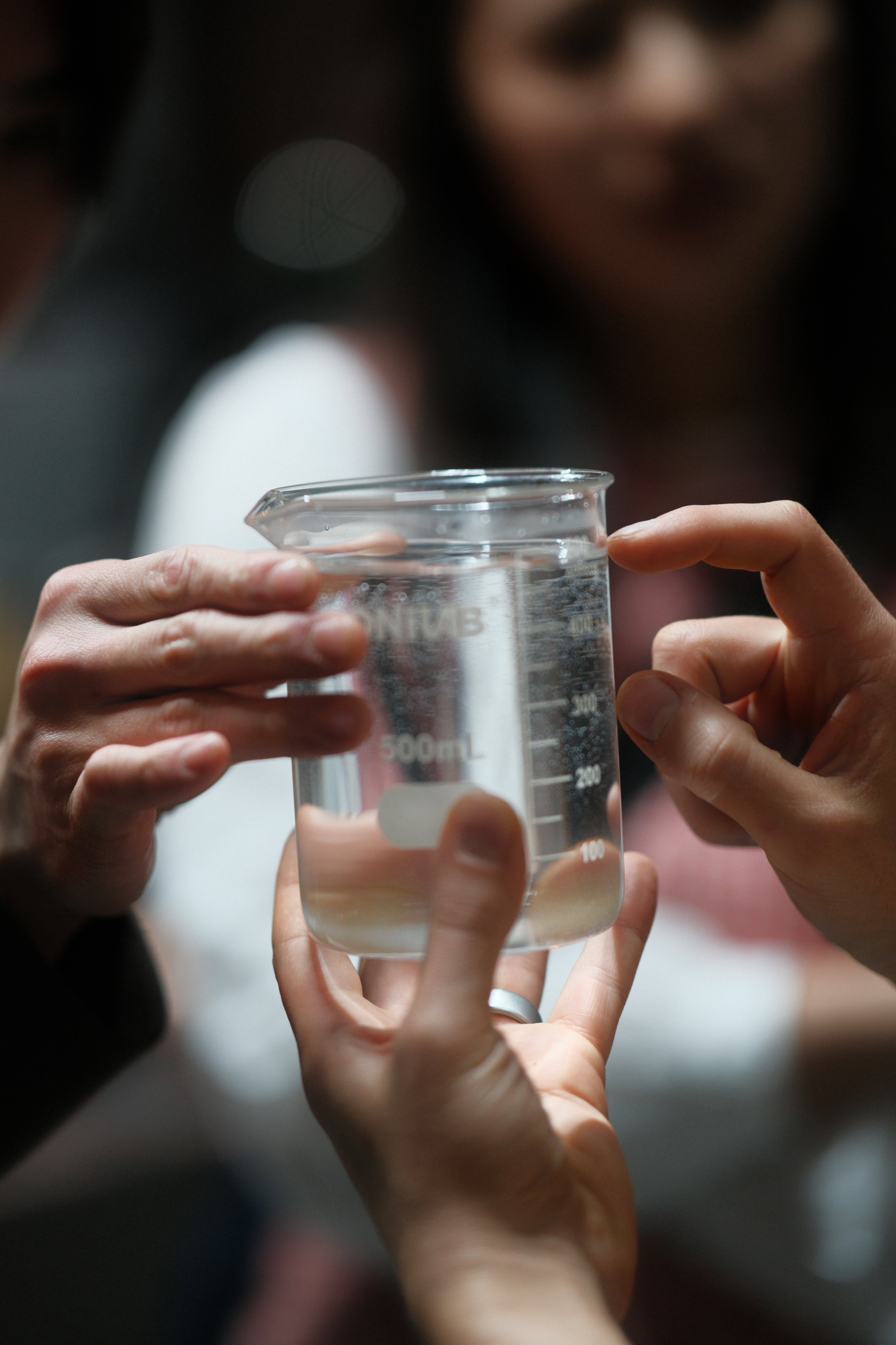 Close-up of hands holding a clear water for coffee glass in a measuring cup with blurred background