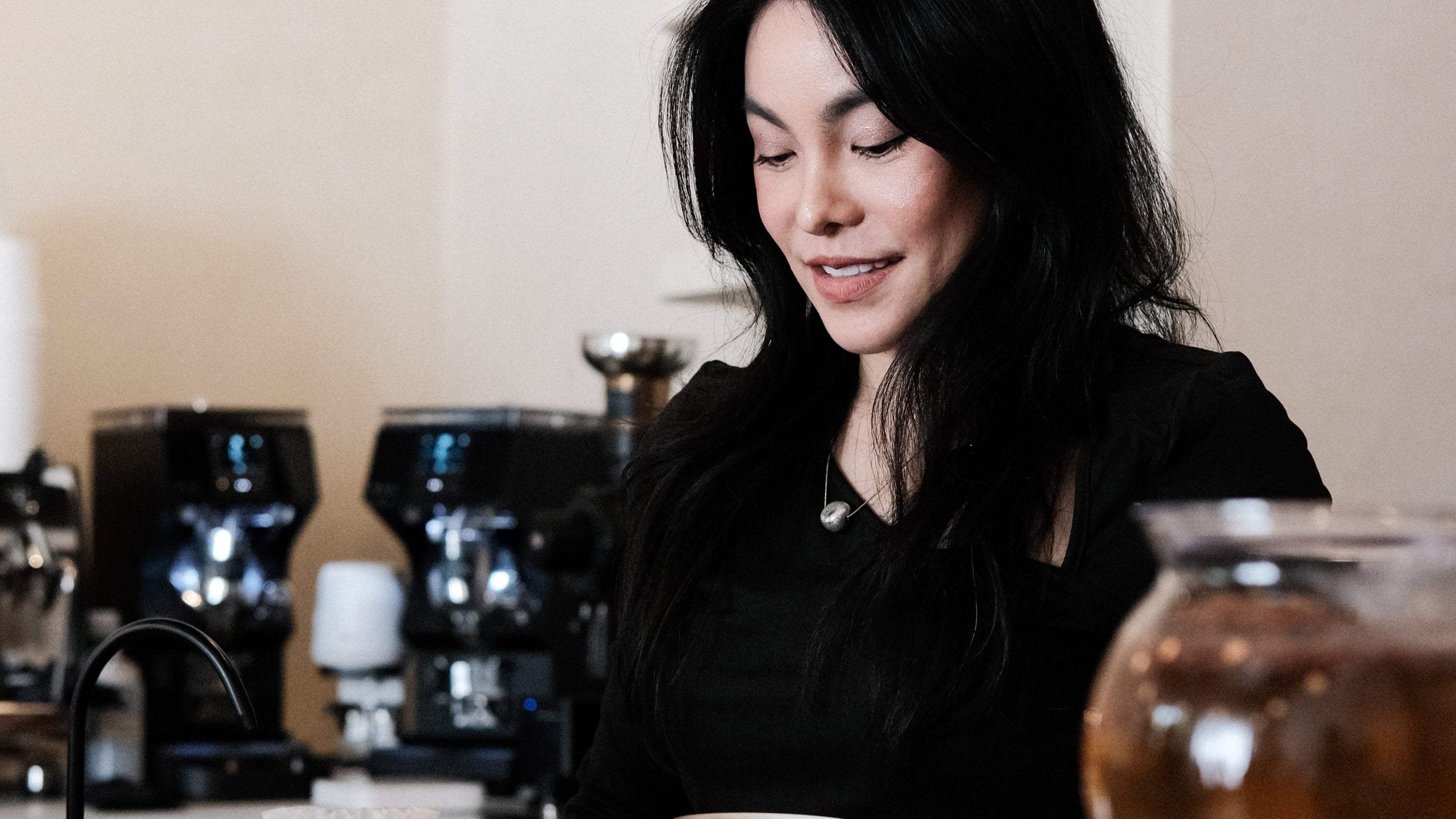 Woman in a coffee shop setting with coffee equipment and a cup.