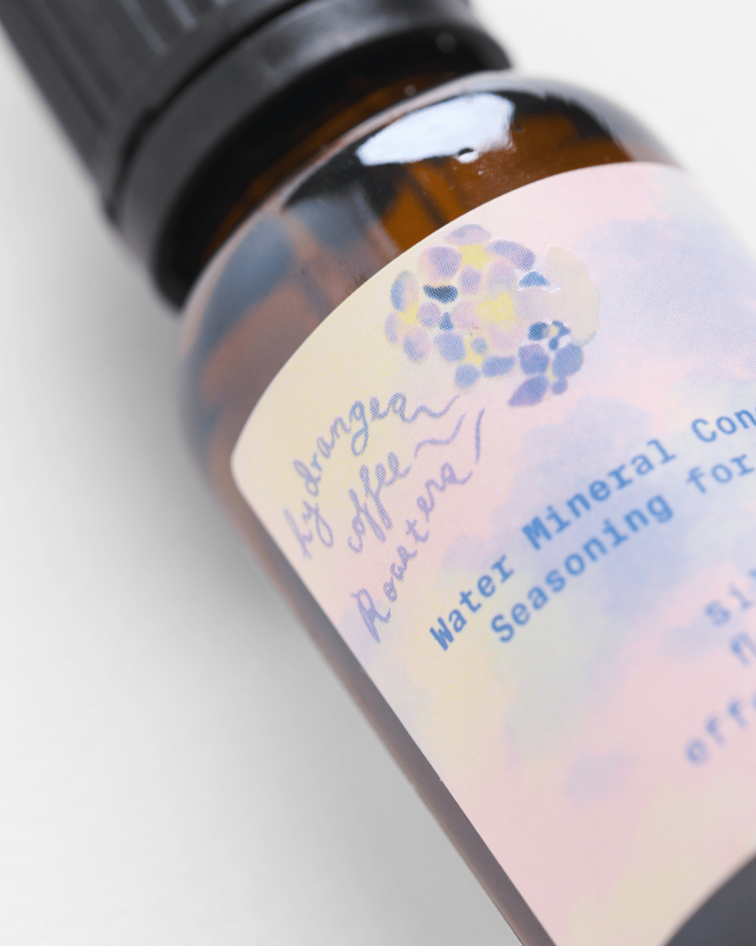 Close-up of an amber glass bottle with a black cap and a pastel label reading 'Hydrangea Coffee Roasters' and 'Water Mineral Concentrate'.