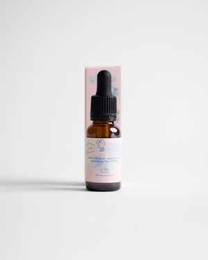 A small amber glass dropper bottle standing in front of a pale pink rectangular box on a clean white studio background.